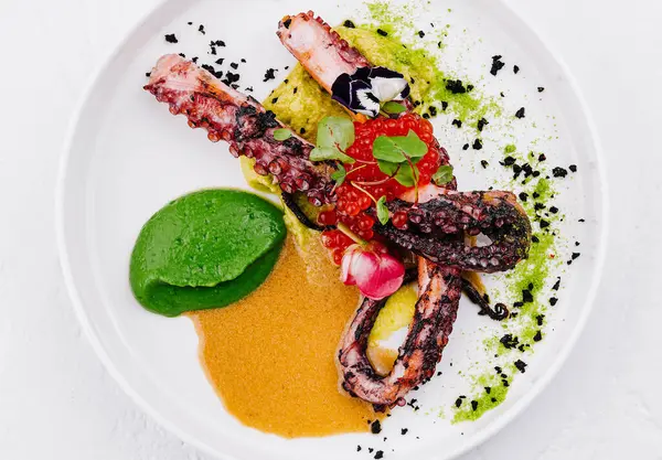 stock image Elegant plated dish of grilled octopus with colorful vegetable purees and seasoning