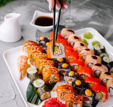 Çeşitli tabaktan suşi rulosu almak için çubuk kullanan birinin yakın plan fotoğrafı.