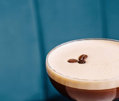 Kahve çekirdeği garnitürlü espresso martini, beyaz bir masada mavi bir arkaplanda servis edilir.