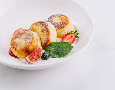 Çilek ve nane şekeriyle süslenmiş üç altın rengi süzme peynir krepi.