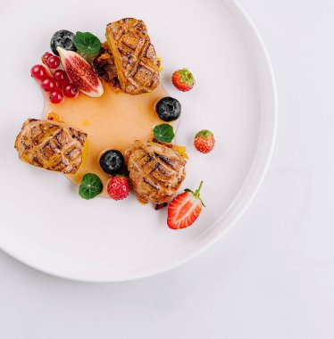 Beyaz arka planda çeşitli böğürtlen ve sos içeren şık bir et tabakasının üst görüntüsü.