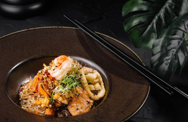 Pürüzsüz bir tabakta servis edilen karides ve otlu deniz ürünleri makarnasının zarif bir sunumu.