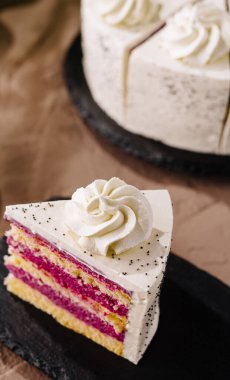 Kremalı ve haşhaş tohumlu zarif bir pasta dilimi, bir tabakta servis edilir.