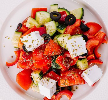 Beyaz bir tabakta servis edilen renkli bir Yunan salatasının üst görüntüsü.