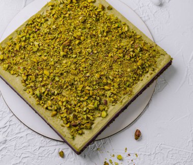 Kahve fincanı, çiçek dekoru ve klasik tatlı çatalıyla beyaz bir tabakta servis edilen enfes şam fıstıklı kek.