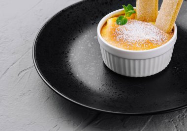 Klasik creme brulee beyaz bir ramekin içinde kadın parmaklarıyla, toz şekerle kaplanmış siyah bir tabakta