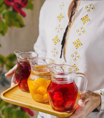 Nakışlı giysiler içinde elinde renkli meyve suyu sürahisi dolu bir tepsi tutan birinin yakın çekimi.