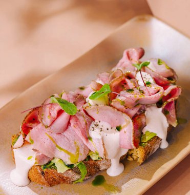 Nefis bir tabakta servis edilen, kabuklu ekmeğin üzerinde otlarla süslenmiş jambon dilimleri.