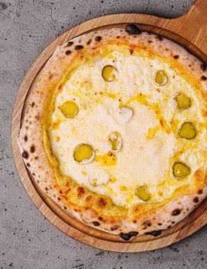 Tahta bir pizza tahtasında servis edilen, turşu soslu, lezzetli bir peynirli pizzanın üst görüntüsü.