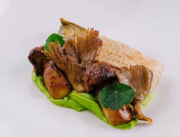 stock image Elegant serving of seared fish over green pea puree with roasted mushrooms on a white plate
