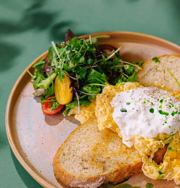 Çırpılmış yumurta, tost ve yeşil bir arka planda servis edilen taze salatadan oluşan sağlıklı bir kahvaltı.