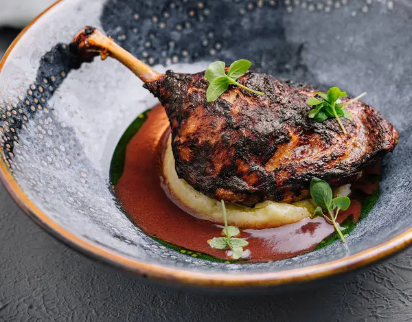 Modern koyu seramik tabakla kremalı pürede servis edilen nefis ördek konfetisi, güzel bir yemek sunumu.