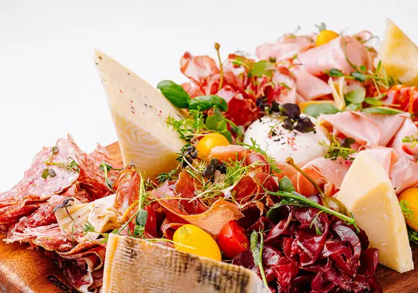 İçinde çeşitli peynirler, pişirilmiş etler ve ahşap bir yüzey üzerindeki süslerin bulunduğu zarif şarküteri tahtası.