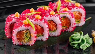 Yanında wasabi ve zencefil ile birlikte siyah bir tabakta balık yumurtası ile süslenmiş nefis suşi ruloları.