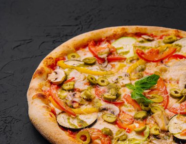 Koyu dokulu yüzeyde çeşitli malzemelerle canlı sebze pizzası.