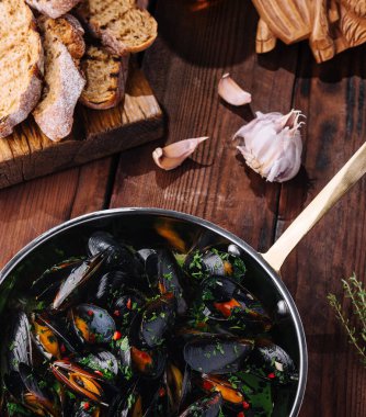 Lezzetli bir bitki sosunda pişirilmiş midye, kırsal bir ahşap masada çıtır ekmekle servis edilir.