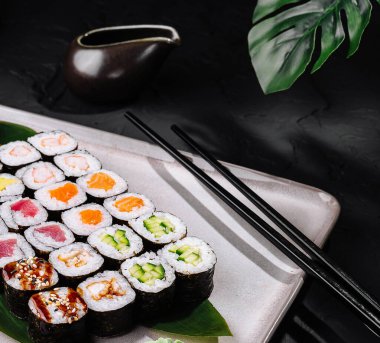 Geleneksel suşi seçimi modern bir tabakta soya sosu ve wasabi ile sunuluyor.