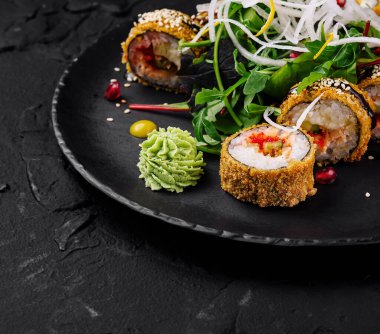 Suşi rulolarının koyu bir arka planda süslerle sunumu.