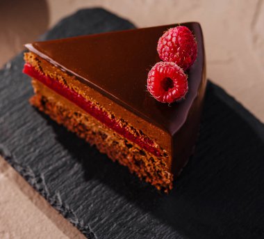 Pastanın yanında ahududu kaplı bir dilim çikolatalı pasta.