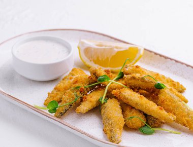 Seramik tabakta limon ve kremalı tartar sosuyla servis edilen balık kroketleri.