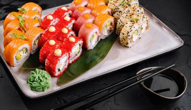 Suşi çeşitleri, siyah arka planda süslerle sanatsal olarak kaplanmış.