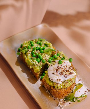 Şık bir tabakta bezelye, tohum ve kremayla süslenmiş zarif avokado tostu.