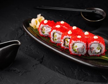 Kırmızı havyarla kaplı zarif suşi rulosu, soya sosu ve sade siyah tabakta wasabi ile servis ediliyor.