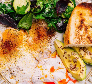 Haşlanmış yumurta, avokado dilimleri ve acı sosla ıslatılmış yeşillikler.