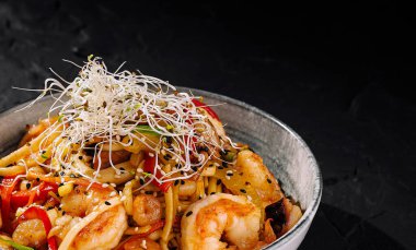 İştah açıcı deniz ürünleri, karides, sebze ve erişteyle kızartılmış, koyu, dokulu bir arka planda servis ediliyor.