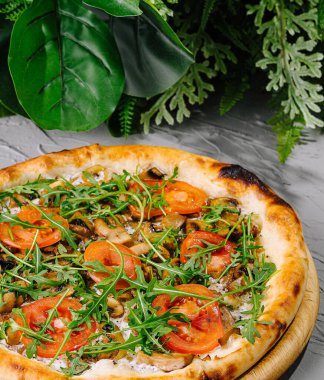 Tahtada taze roka, domates ve peynirli vejetaryen pizza.