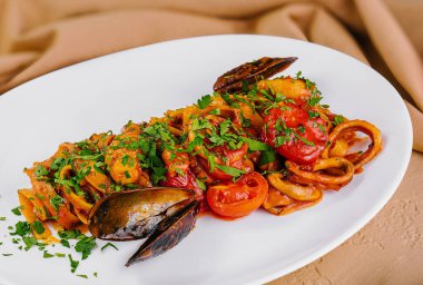 Carbonara soslu spagetti ve beyaz tabakta otlarla süslenmiş domatesli deniz ürünleri makarna tabağı.