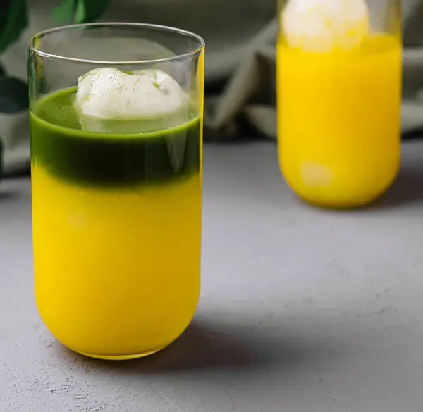 stock image Vibrant green matcha float beside a glass of fresh mango juice on a chic grey background