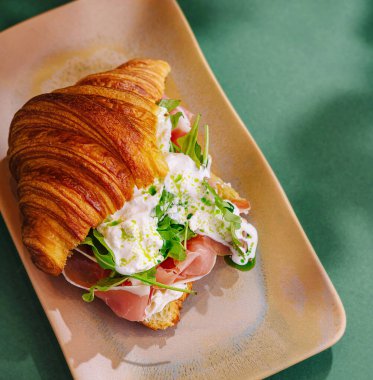 Nefis bir tabakta prosciutto, krem peynir ve roka ile taze yapılmış kruvasan sandviçi.