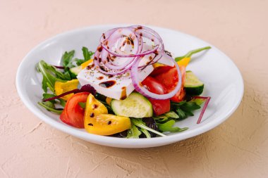 Renkli ve sağlıklı Yunan salatası ve beyaz peynir. Taze sebzeler. Ve beyaz tabakta yapraklı yeşillikler. Domatesli lezzetli ve besleyici bir vejetaryen yemeği. Salatalık. Soğan. Dolmalık biber