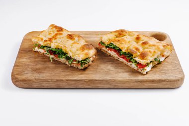 Kesme tahtasının üzerinde sebze ve peynirli dilimlenmiş İtalyan panini, beyaz arka planda izole edilmiş.