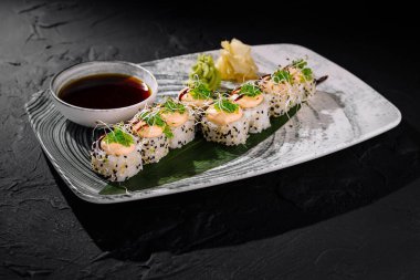 Karidesli gurme suşi rulosu, mikro yeşilliklerle süslenmiş, soya sosu ve wasabi ile servis edilmiş şık bir tabakta