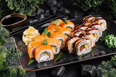 Fresh sushi rolls with salmon and eel on a modern black plate, served with soy sauce