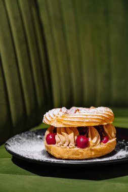 Siyah tabakta krema ve böğürtlen ile yeşil arka planda lezzetli Paris-Brest.