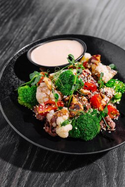 Karnabahar, brokoli ve soslu siyah bir tabakta biber ile renkli sebze kızartması.