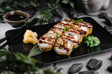 İştah açıcı tempura suşi rulosu siyah bir tabakta servis edilir, baharatlı çiseleme ve süslemelerle süslenir.