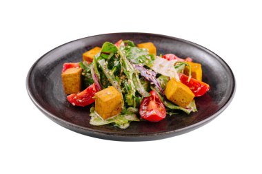 Tofulu, domatesli renkli vejetaryen salatası, ve siyah bir tabakta yeşiller, beyaz arka planda izole edilmiş.