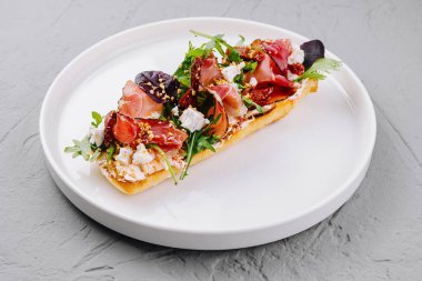 Beyaz bir tabakta prosciutto, feta, domates ve roka ile süslenmiş nefis bruschetta.