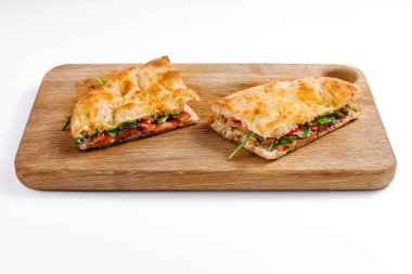 Domatesli, peynirli ve yeşillikli nefis bir panini sandviçi var. Tahta kesme tahtasının üzerinde kesilip servis ediliyor.