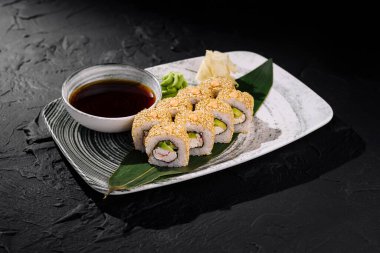 Koyu arkaplanda soya sosu ile servis edilen susam tohumları serpiştirilmiş California rulolarının zarif sunumu