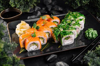 Soya sosuyla servis edilen, siyah bir tabakta somonla servis edilen zarif suşi rulo seçimi.