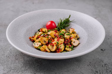 Seramik kasede kiraz domatesi ile süslenmiş taze sotelenmiş mantarlar.