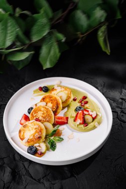 Beyaz bir tabakta çilek ve meyve sosuyla süslenmiş peynirli krepler sundum.