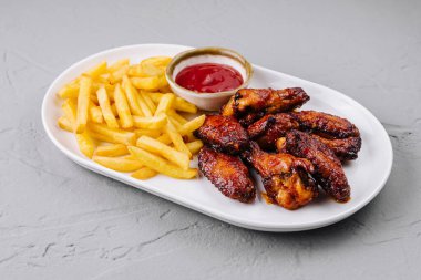 Lezzetli kızarmış tavuk kanatları, yanında patates kızartması ve beyaz tabakta ketçap.