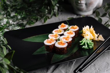 Yeşil yapraklı siyah tabakta sofistike suşi düzenleme, mutfak sunumları için mükemmel.