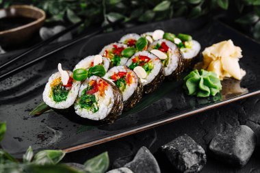 Elegant sushi rolls with fresh ingredients on a black slate background, garnished with greens